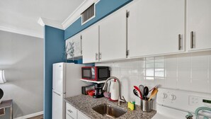Une cuisine compacte avec des meubles blancs, un four à micro-ondes, une bouilloire et un évier.