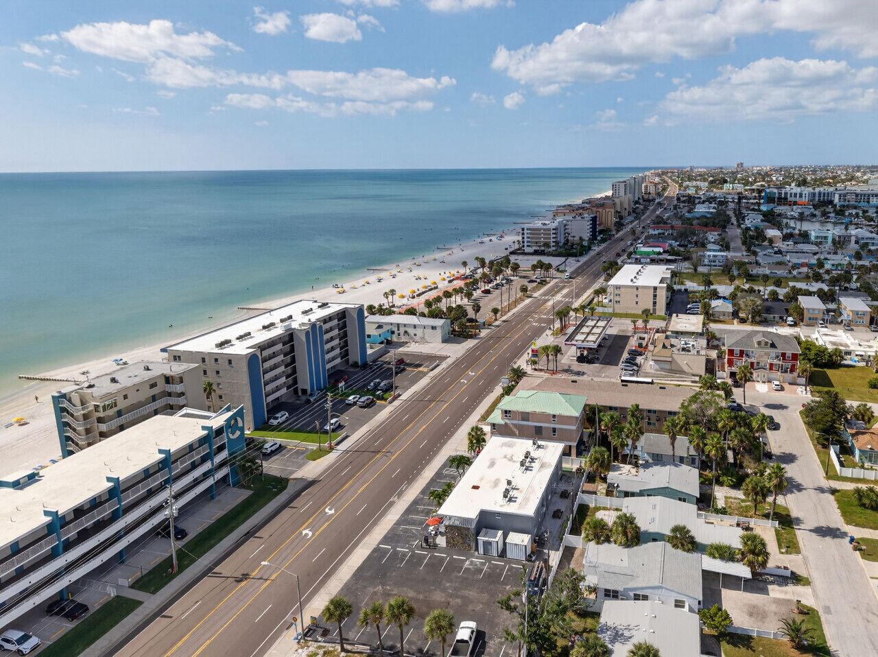 An aerial view of a coastal city with a beach, a parking structure, and a mix of residential and commercial buildings.