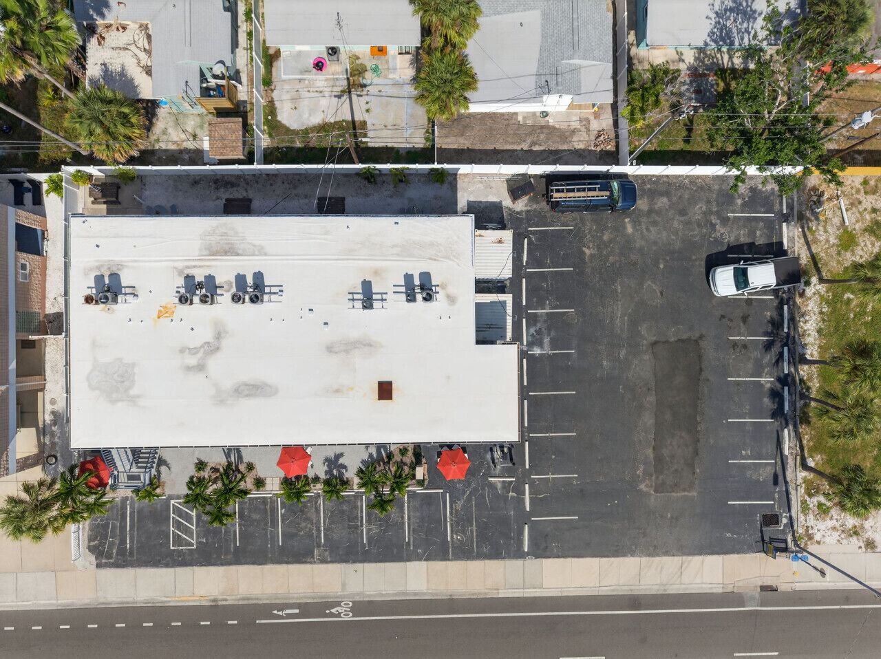 An aerial view of a parking lot with a large building in the background, surrounded by trees and a road.