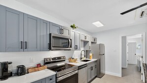 A modern kitchen with grey cabinets, stainless steel appliances, and a white countertop.