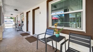 A covered corridor with a bench, chairs, and a potted plant.