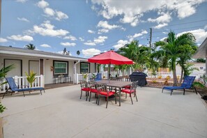 A covered patio area with a table and chairs, a red umbrella, and a barbecue grill.