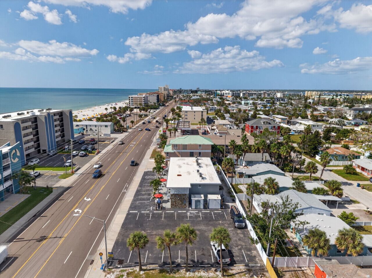 An aerial view of a coastal town with a beach, buildings, and a road.