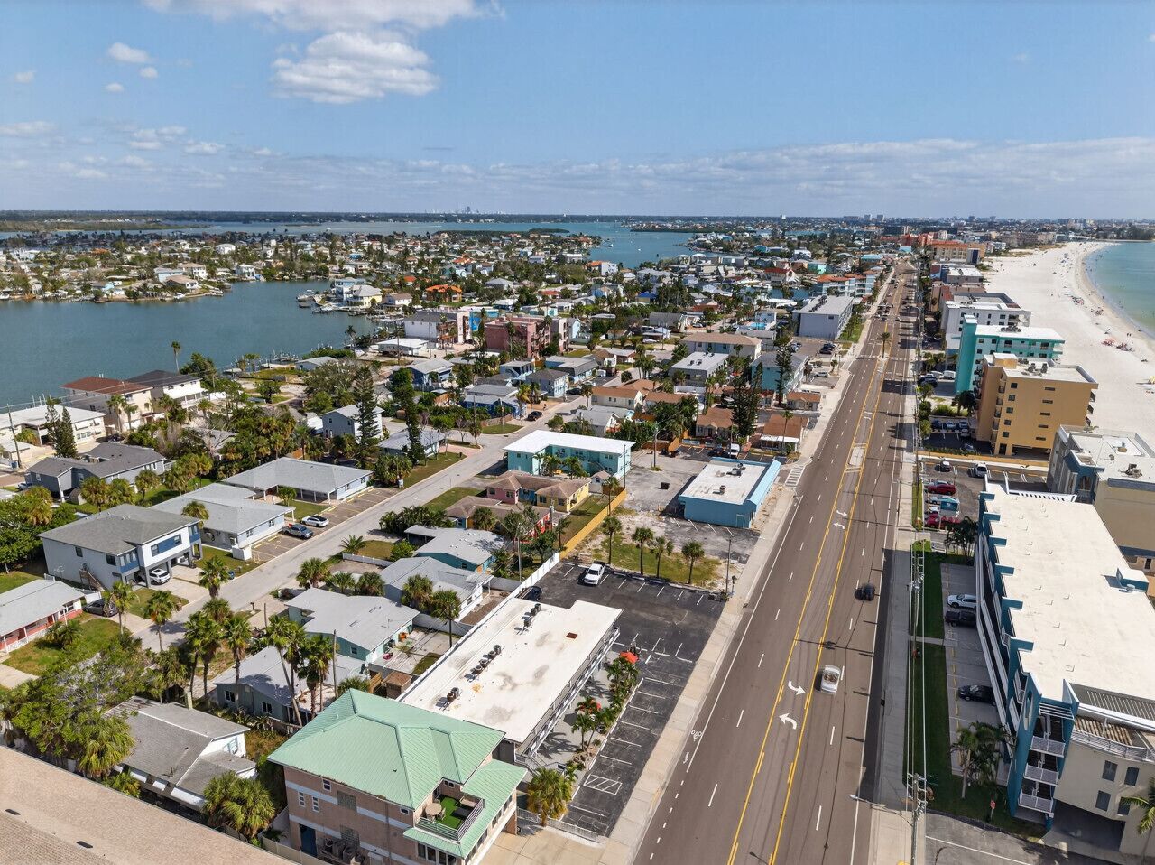 Vue aérienne d’une ville côtière avec une plage, des immeubles résidentiels et une route principale.