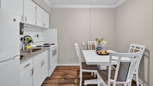 Una cocina compacta con gabinetes blancos, un horno y un comedor con mesa y sillas.