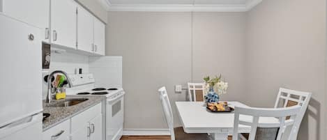 Una cocina compacta con gabinetes blancos, un horno y un comedor con mesa y sillas.