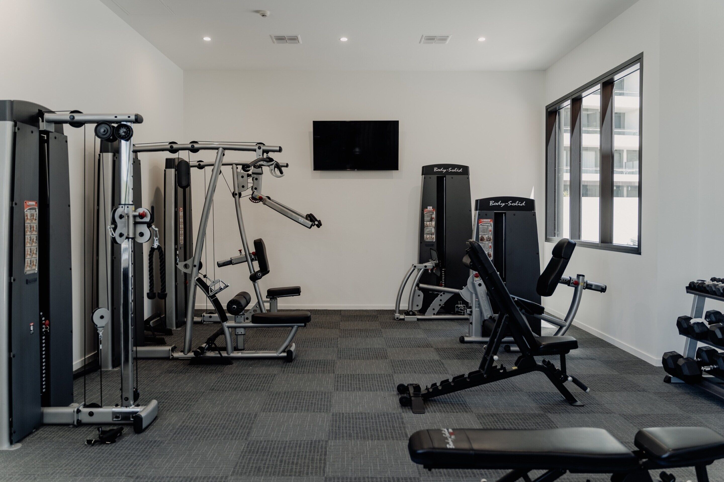 A gym with various exercise equipment, a television, and a window providing natural light.