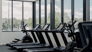 A gym with treadmills and exercise equipment, large windows, and a view of trees and buildings. - Cosy 1-bed With Pool, Gym ,parking (Canberra)