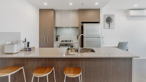 A modern kitchen with a central island, bar stools, a refrigerator, and a stove. - Cosy 1-bed With Pool, Gym ,parking (Canberra)