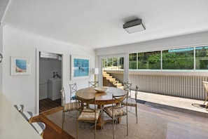 A modern dining area with a round wooden table and chairs, a view of a balcony with a railing, and a staircase leading to an upper level.