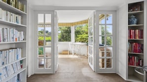 A room with open doors leading to a conservatory, a bookshelf, and a table with chairs. - Poolside Stay - Close to Taronga Zoo & Luna Park (Sydney)