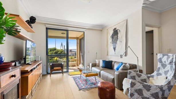 A modern living room with a sofa, armchair, and coffee table. There is a kitchen area with a dining table and chairs. A large window provides a view of the outdoors. - Elegant Stay in Balmain With Pool Access (Sydney)