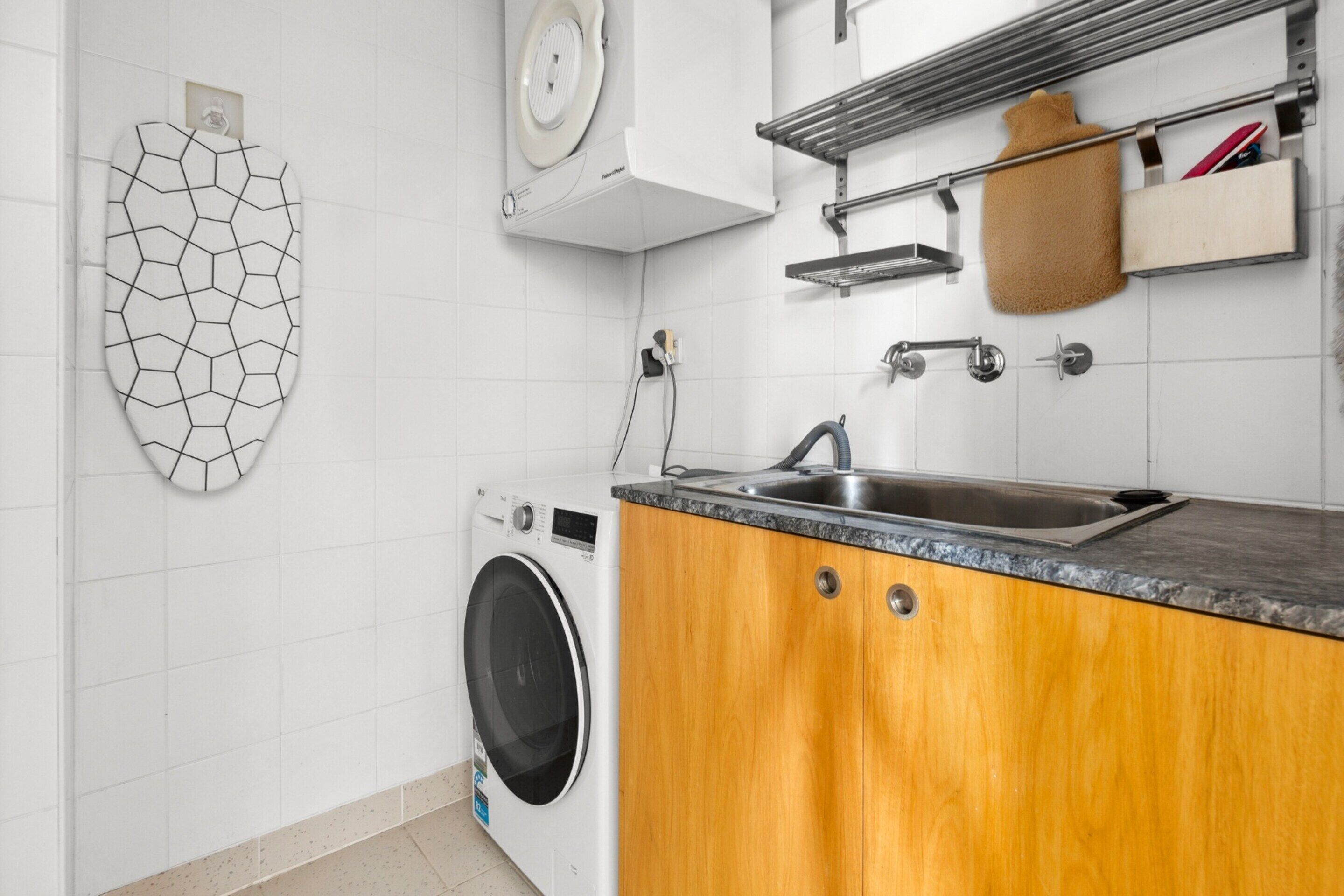 A kitchen with a washing machine, a sink, wooden cabinets, and a towel rack.