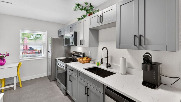 A modern kitchen with grey cabinets, a microwave, a sink, and a coffee machine. - 🌴 Updated1BR at Park Shore Suites | Steps to Madeira Beach | Courtyard & Grill 🌅 (Madeira Beach)