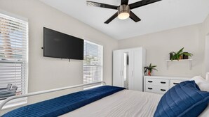 A bedroom with a bed, a ceiling fan, a TV mounted on the wall, a wardrobe, and a small plant on a shelf. - 🌴 Updated1BR at Park Shore Suites | Steps to Madeira Beach | Courtyard & Grill 🌅 (Madeira Beach)