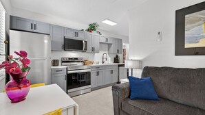 A modern kitchen with grey cabinets, a microwave, an oven, and a dining area with a white table and yellow chairs. - 🌴 Updated1BR at Park Shore Suites | Steps to Madeira Beach | Courtyard & Grill 🌅 (Madeira Beach)