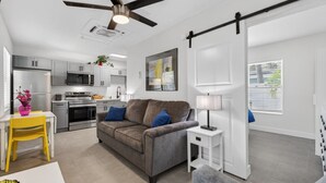 A modern living room with a grey sofa, a white side table, and a yellow chair. There is a kitchen in the background with white cabinets and stainless steel appliances. - 🌴 Updated1BR at Park Shore Suites | Steps to Madeira Beach | Courtyard & Grill 🌅 (Madeira Beach)