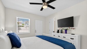 A bedroom with a bed, a ceiling fan, a TV, a dresser, and a window with blinds. - Modern 2BR at Park Shore Suites | Walk to Madeira Beach | Courtyard & Grill (Madeira Beach)