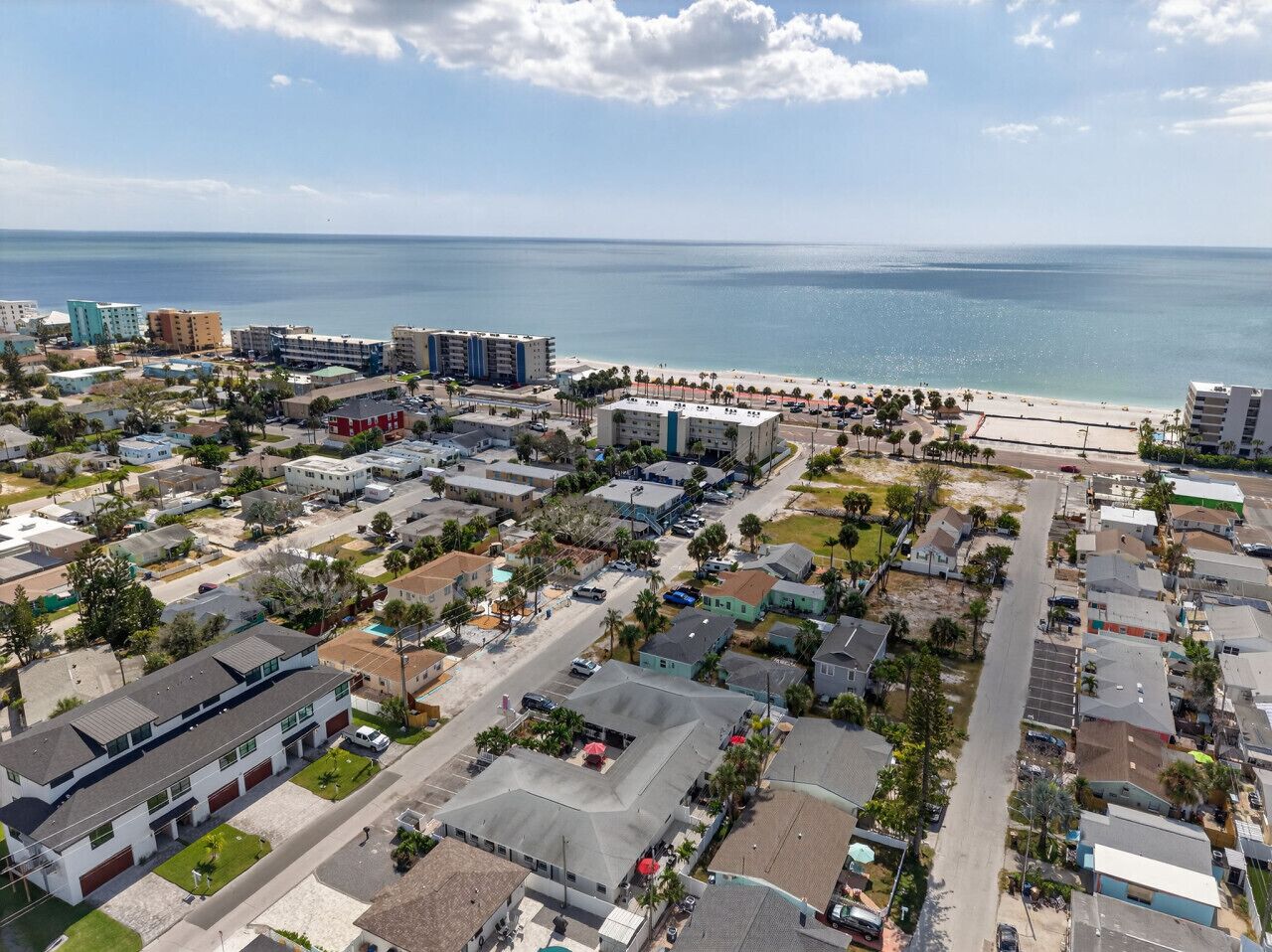 An aerial view of a coastal town with a beach, residential buildings, and a marina.