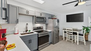 A modern kitchen with grey cabinets, stainless steel appliances, a microwave, a refrigerator, and a dining area with a table and chairs. - Modern 2BR at Park Shore Suites | Walk to Madeira Beach | Courtyard & Grill (Madeira Beach)
