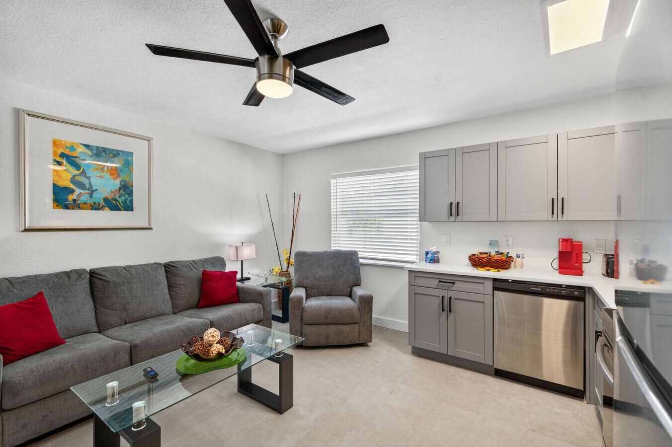 A modern living room with a gray sofa, a glass coffee table, a gray armchair, and a ceiling fan.