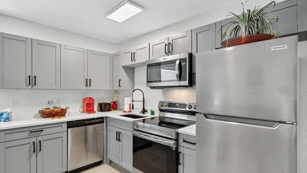 A modern kitchen with grey cabinets, a stainless steel refrigerator, a microwave, an oven, and a dishwasher. - Modern 2BR at Park Shore Suites | Walk to Madeira Beach | Courtyard & Grill (Madeira Beach)