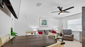 A modern living room with a dining table, sofas, a ceiling fan, and a painting on the wall. - Modern 2BR at Park Shore Suites | Walk to Madeira Beach | Courtyard & Grill (Madeira Beach)