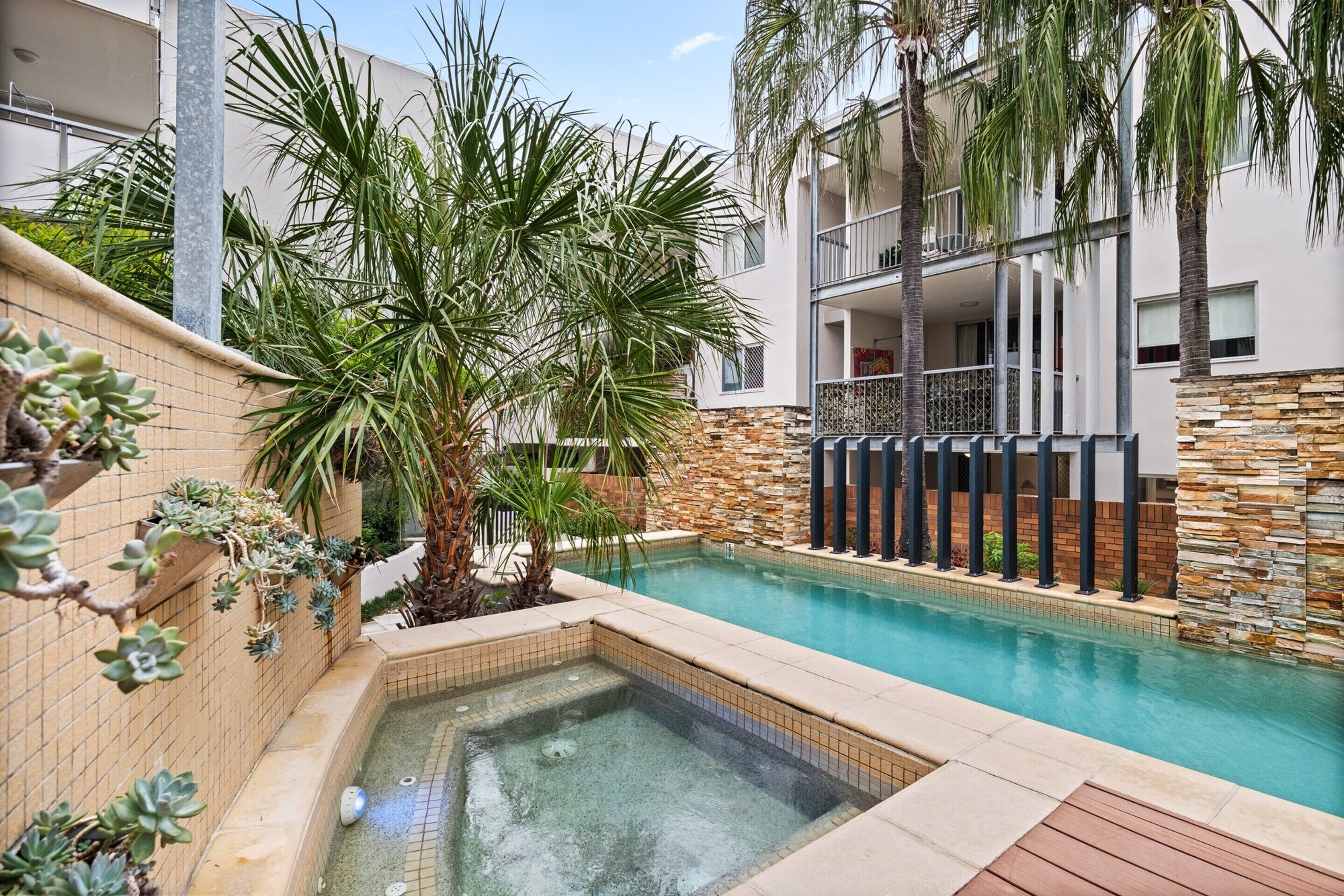 Un área de piscina con jacuzzi, rodeada de palmeras y un muro de piedra.