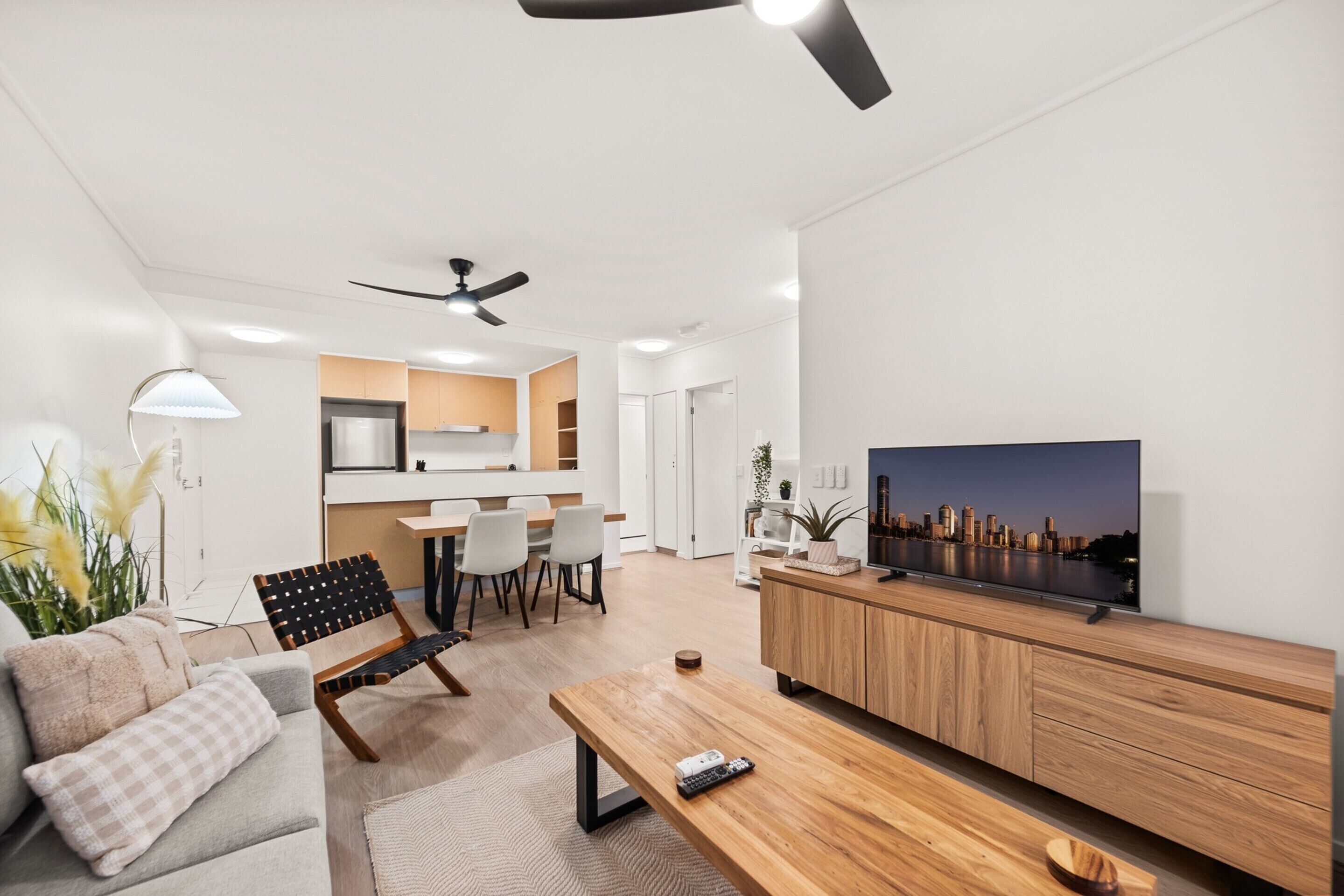 A modern living room with a sofa, a wooden coffee table, a TV on a wooden cabinet, and a ceiling fan.