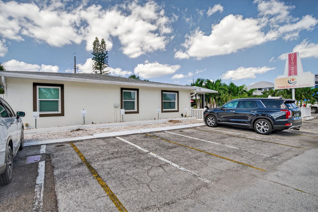 A building with a sign for 'Park Shore Suites' and a parking lot with a black SUV.