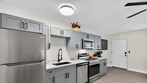 Una cocina moderna con armarios grises, electrodomésticos de acero inoxidable y una encimera blanca.