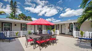 A patio area with a table and chairs, a red umbrella, and a white fence.