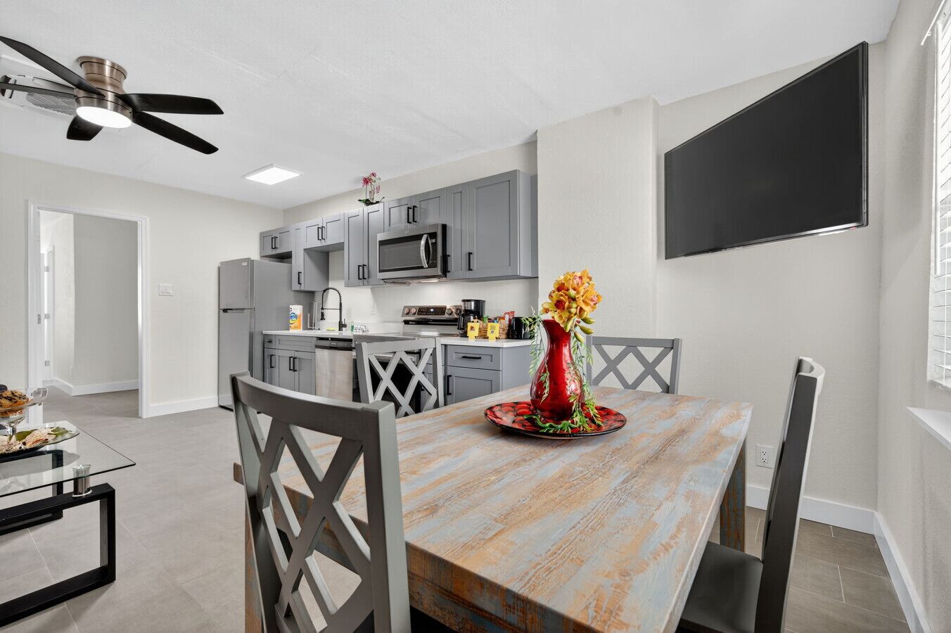 Een moderne keuken met grijze kastjes, een magnetron en een eethoek met een houten tafel en stoelen.