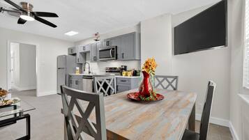 Een moderne keuken met grijze kastjes, een magnetron en een eethoek met een houten tafel en stoelen.