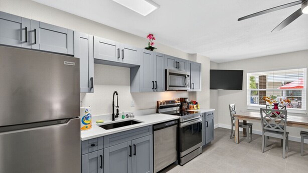A modern kitchen with grey cabinets, stainless steel appliances, and a window with a view of the outdoors.