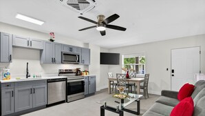 A modern kitchen with grey cabinets, a microwave, and a dishwasher. There is a dining area with a table and chairs, and a grey sofa with red cushions.