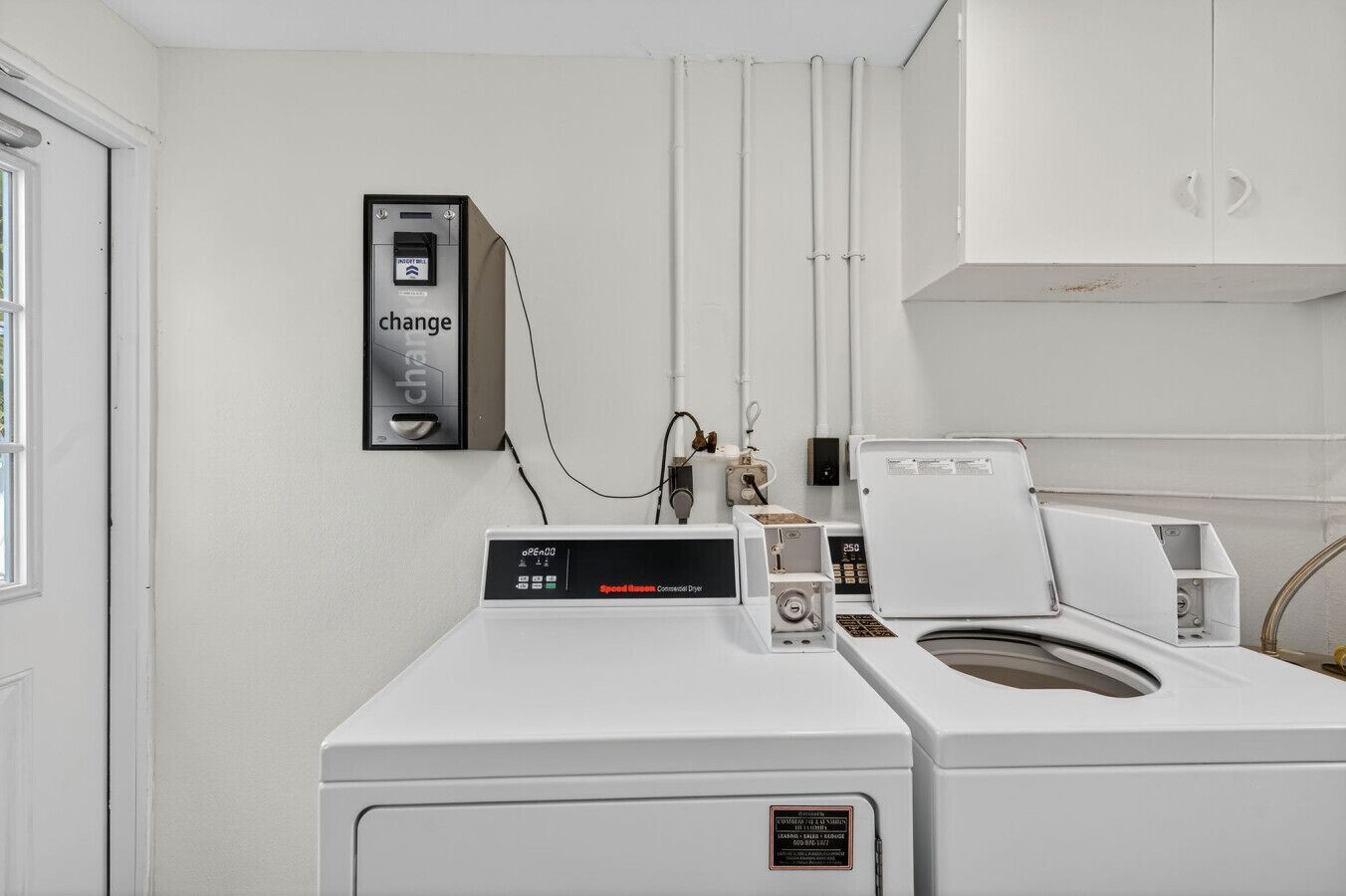 A laundry room with a front-loading washing machine, a wall-mounted dryer, and a change machine.