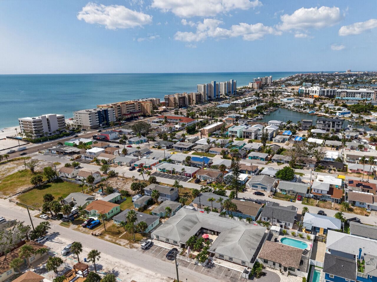 Vue aérienne d’un quartier résidentiel situé sur la côte, avec un mélange de maisons unifamiliales et d’immeubles à plusieurs étages, un port de plaisance et une plage en arrière-plan.