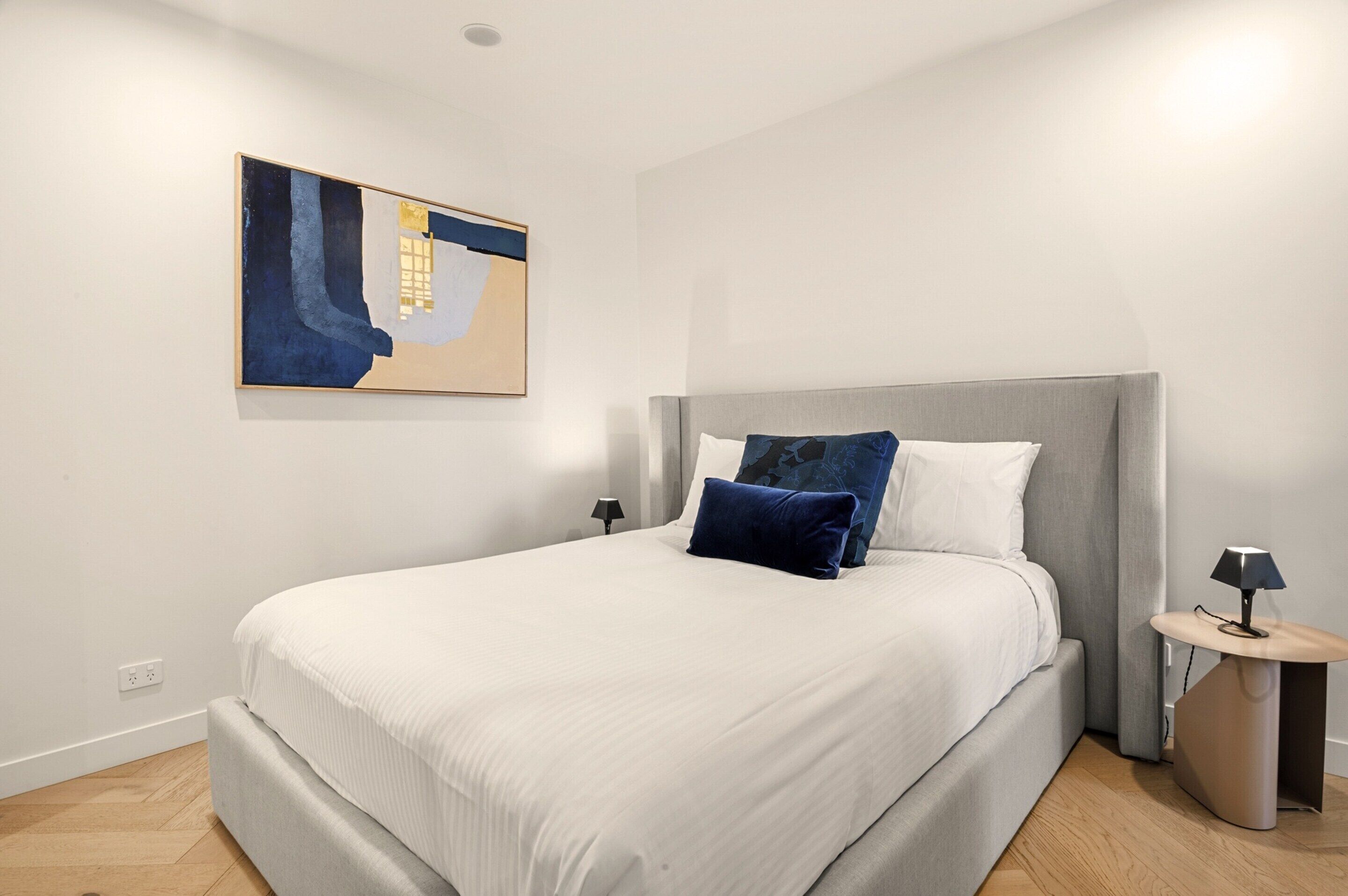 Un dormitorio moderno con una cama grande, cabecera, mesita de noche y un cuadro abstracto colgado en la pared.