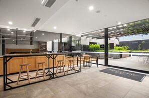 A modern kitchen with a bar area, large windows, and a patio with outdoor seating. - Bright 2-bed Apartment in Fitzroy's Heart (Melbourne)