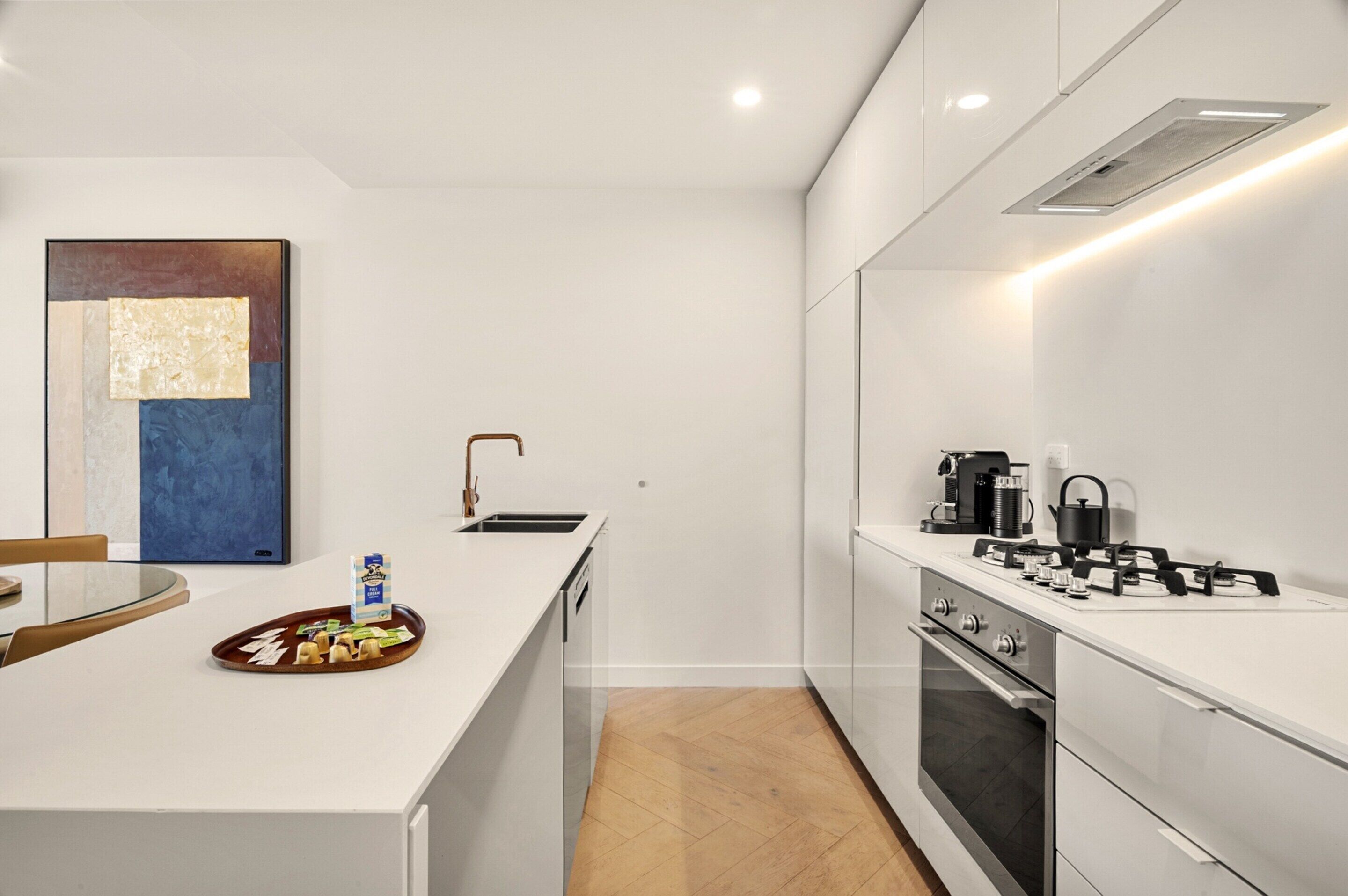A modern kitchen with white cabinetry, a built-in stove, and a coffee maker.
