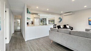 A modern kitchen with white cabinets, a grey sofa, and a dining area with a view.