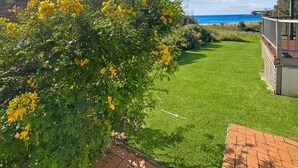 A well-maintained lawn with a view of the ocean, a wooden deck, and a brick wall.