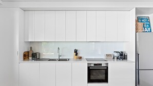 A modern kitchen with white cabinets, a stainless steel refrigerator, a built-in oven, and a coffee maker. - Ocean Views, Deck and Parking at Beach Apartment (Sydney)