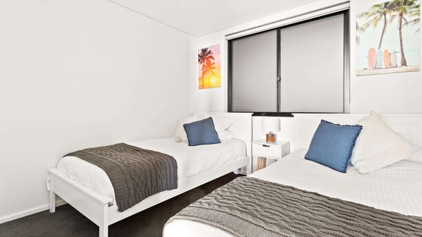 A hotel room with two single beds, a large window, a flat-screen TV, and a small bedside table with a lamp. - Ocean Views, Deck and Parking at Beach Apartment (Sydney)