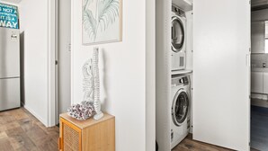 A laundry room with a washing machine and dryer, a wooden cabinet with decorative items, and a wall with a framed plant and a motivational quote. - Ocean Views, Deck and Parking at Beach Apartment (Sydney)