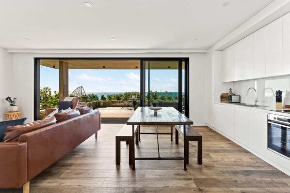 A modern kitchen with a dining area, large windows, and a view of the outdoors. - Ocean Views, Deck and Parking at Beach Apartment (Sydney)
