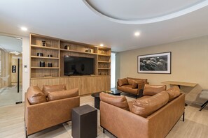 A modern living room with leather sofas, a flat-screen TV, and built-in wooden shelving.