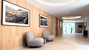 Een moderne hotellobby met houten lambrisering, twee grijze fauteuils, een kleine ronde tafel en lijstwerken aan de muren.