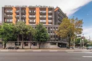 Un hotel de varios pisos con balcones, una entrada a nivel de calle y un área de estacionamiento.